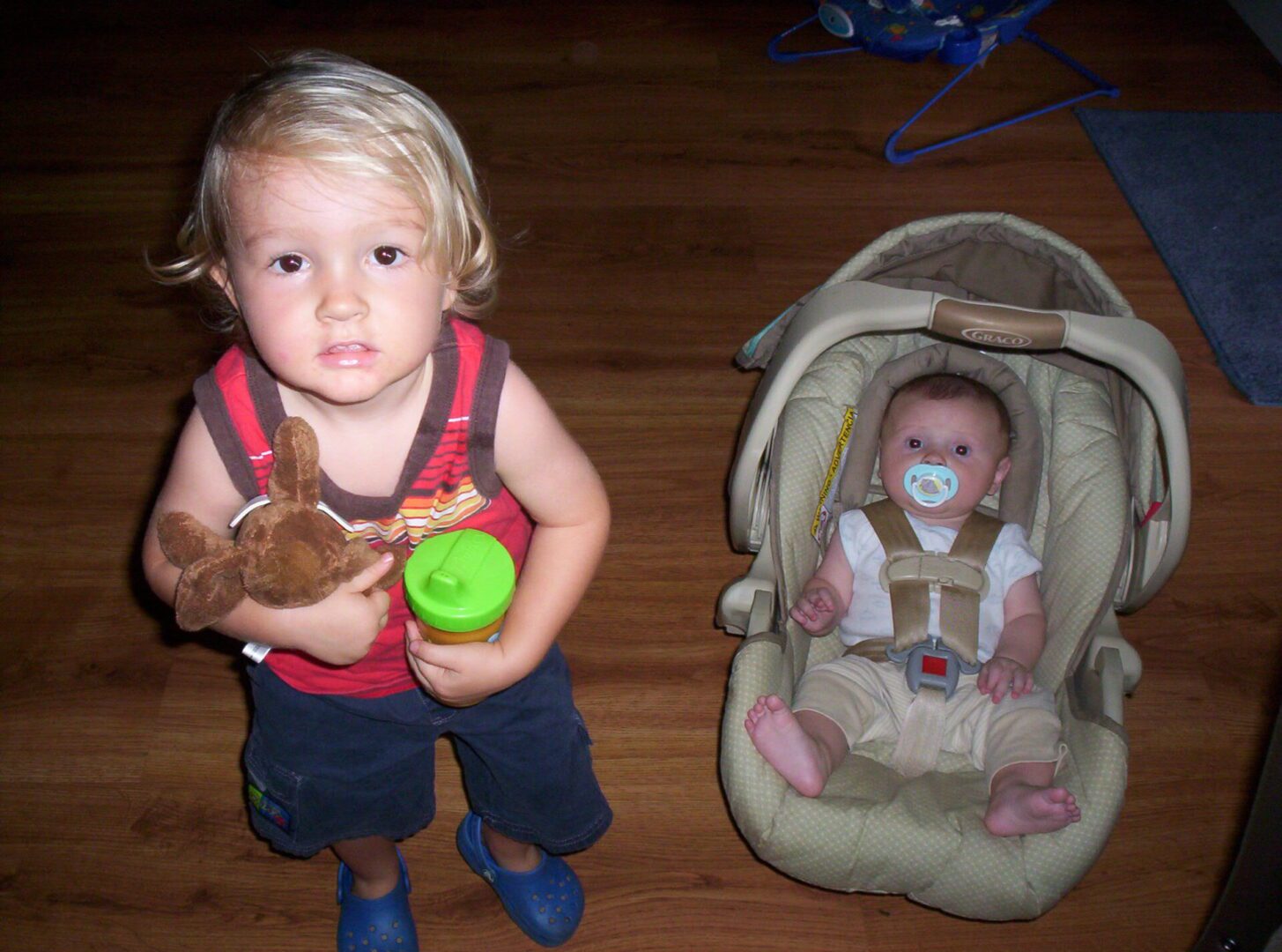 A young child holding a stuffed animal next to a baby in a car seat.